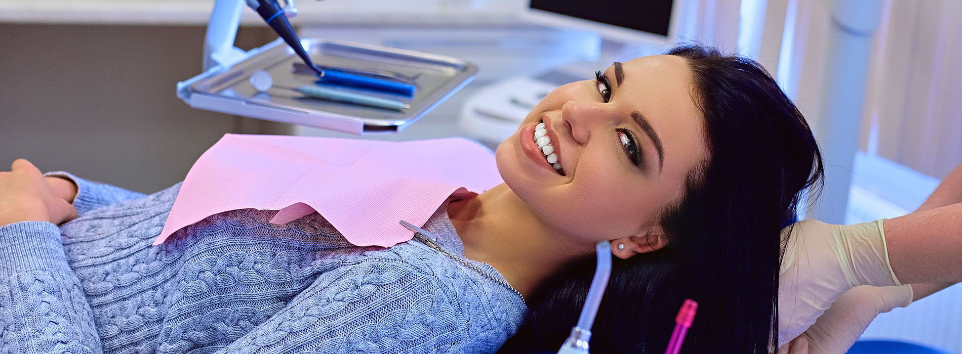 A person is seated in a dental chair, receiving care from a dental professional who stands behind them.