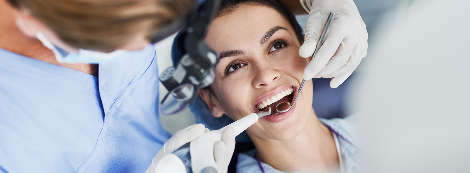 Dental professional performing oral examination on patient with open mouth, in dental office setting.