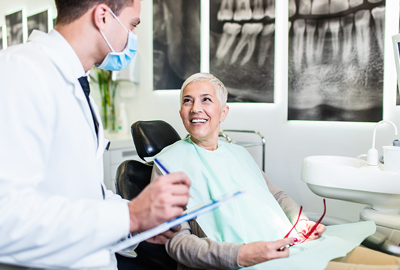 A dentist is assisting a patient in a dental office, with the patient smiling and holding up a toothbrush.