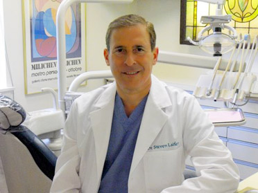 The image shows a man sitting at a dental chair, wearing a white lab coat and stethoscope, suggesting he is a dentist.