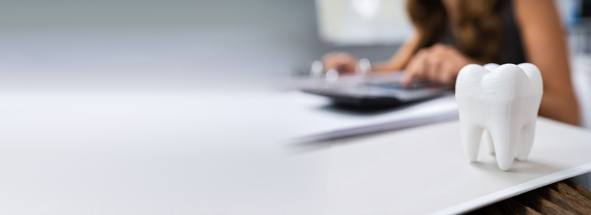 The image shows a person sitting at a desk, working on a laptop with a small figurine resembling a tooth in front of them.